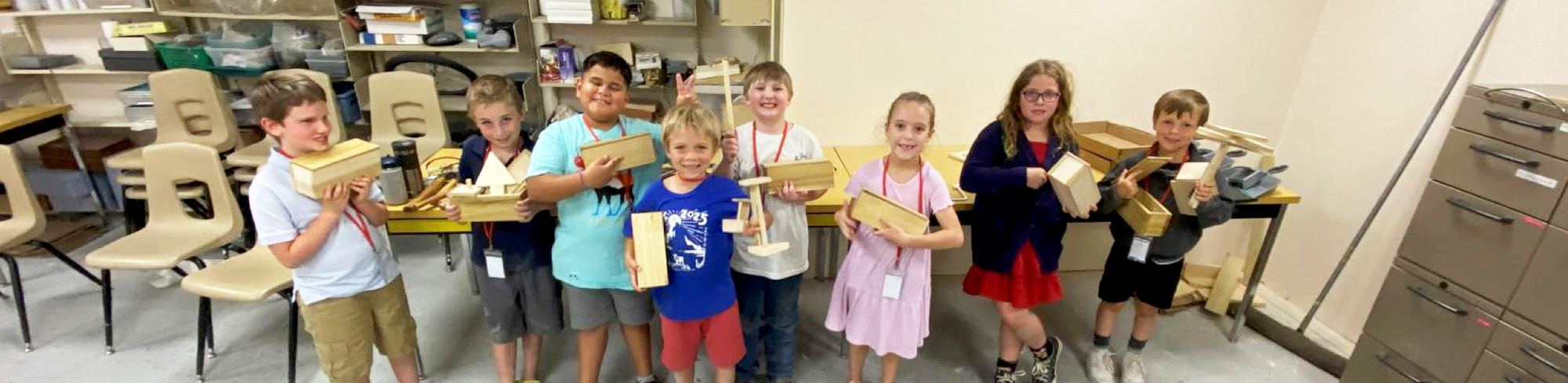 Happy elementary students holding up woodworking projects