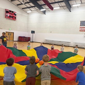 Preschool students playing with a parachute in the gym