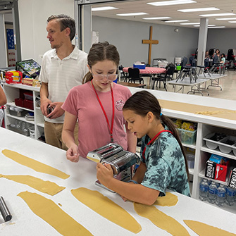Students and an adult working with a pasta machine
