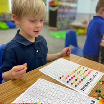 Happy boy working on a colorful math worksheet from his desk